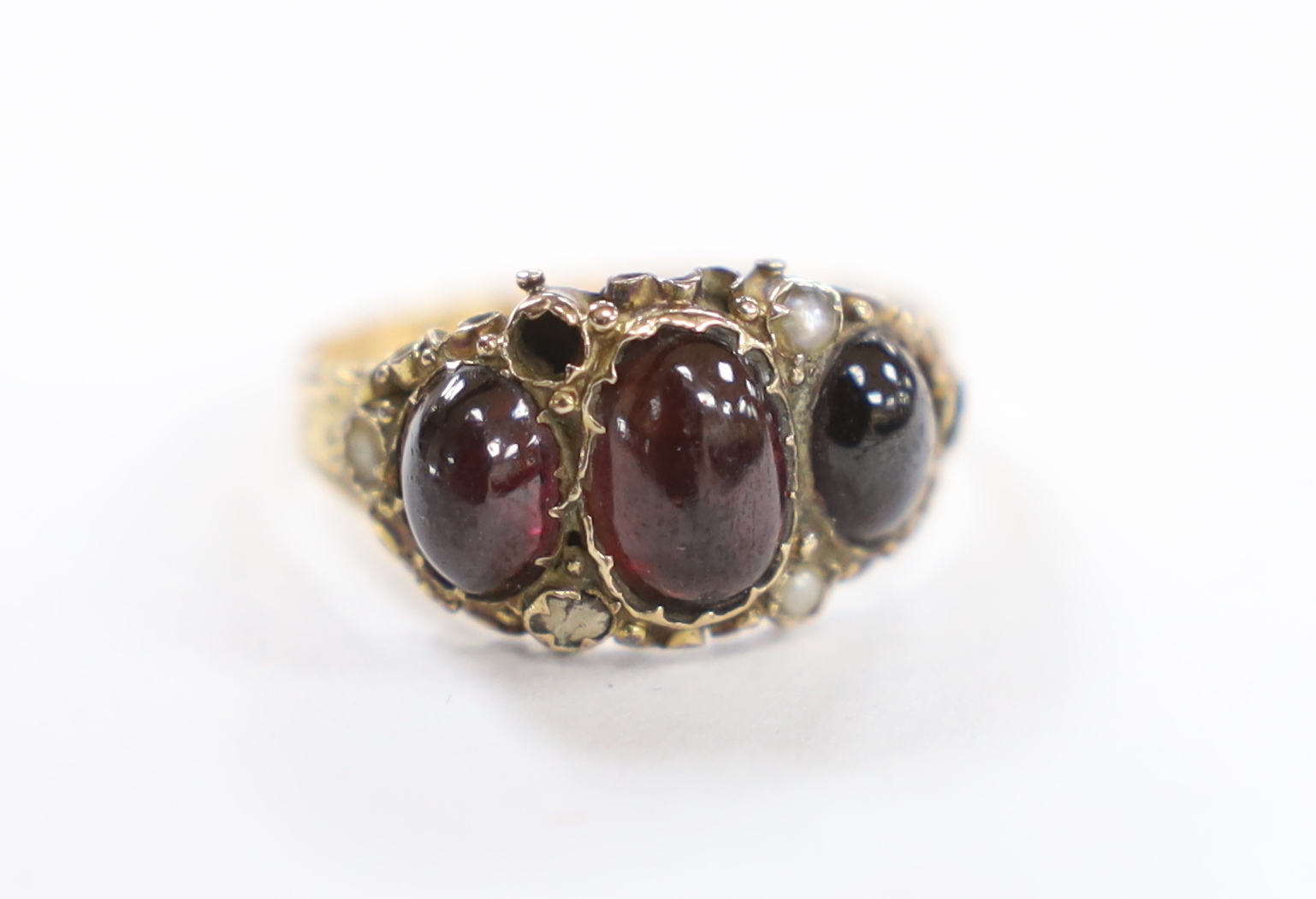 A Victorian 15ct gold, foil backed three stone cabochon garnet and seed pearl cluster set half hoop ring, size O, gross weight 3 grams.